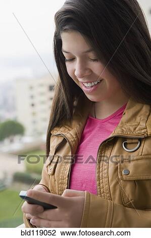 Stock Image - Hispanic girl using cell phone outdoors. Fotosearch