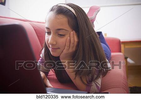 Stock Photography - Hispanic girl using laptop on sofa. Fotosearch