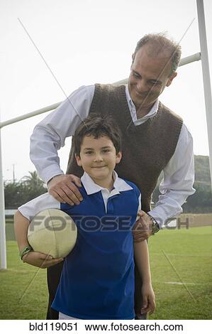 Stock Image - Hispanic man smiling with son on field. Fotosearch