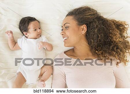 Picture - Hispanic mother and infant laying on bed. Fotosearch