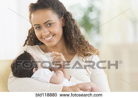 Stock Image - Hispanic mother bottle feeding infant son. Fotosearch