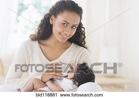 Stock Image - Hispanic mother bottle feeding infant son. Fotosearch