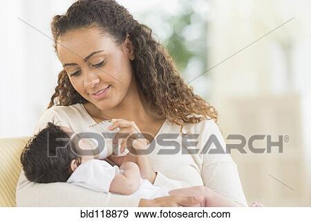 Stock Photo - Hispanic mother bottle feeding infant son. Fotosearch