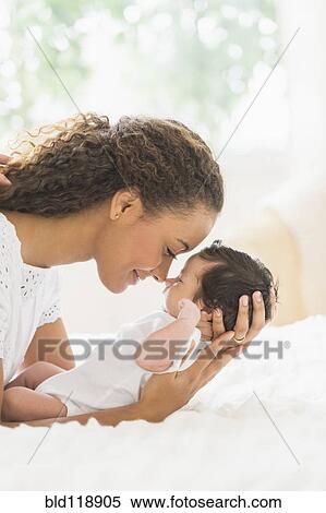 Stock Photography - Hispanic mother holding infant on bed. Fotosearch