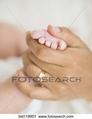 Stock Photo - Hispanic mother holding infant's foot. Fotosearch