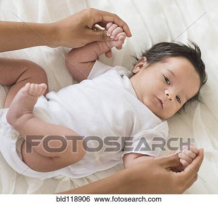 Stock Photograph - Hispanic mother playing with infant on bed. Fotosearch