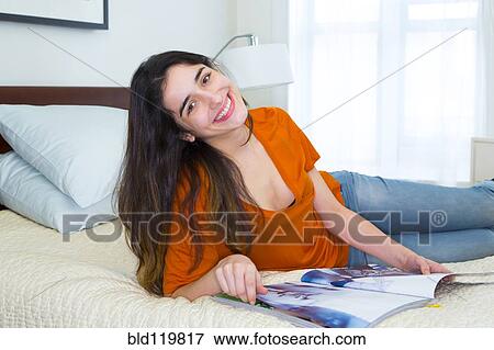 Stock Photo - Hispanic woman reading magazine on bed. Fotosearch