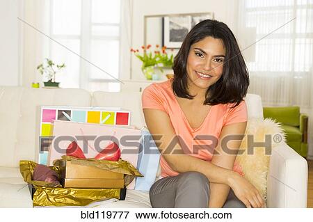 Stock Photo - Hispanic woman sitting on sofa next to birthday gifts. Fotosearch