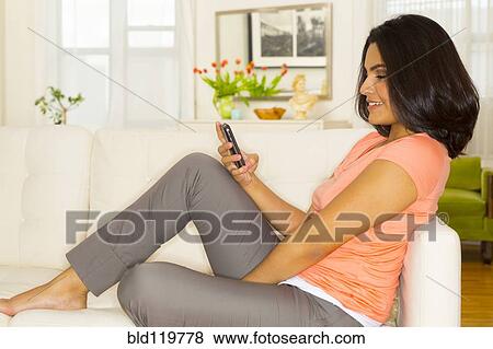 Hispanic woman using cell phone on sofa View Large Photo Image Stock Photo - Hispanic woman using cell phone on sofa. Fotosearch