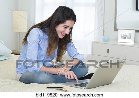 Stock Image - Hispanic woman using laptop on bed. Fotosearch