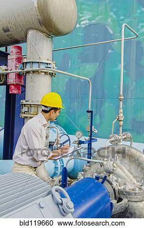 Stock Image - Hispanic worker checking machinery. Fotosearch