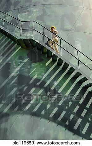 Stock Photo - Hispanic worker climbing water tower. Fotosearch