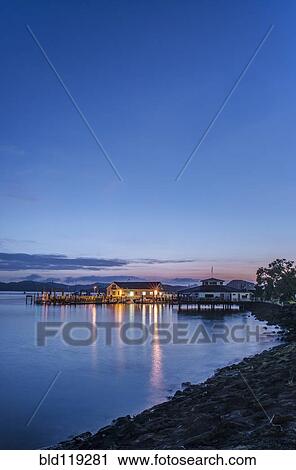 Stock Image - Illuminated buildings on water at dawn. Fotosearch
