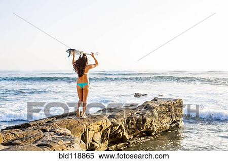 Stock Photography - Japanese woman carrying surfboard on beach. Fotosearch