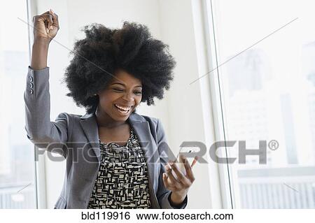 Stock Photograph - Mixed race businesswoman holding cell phone and cheering. Fotosearch