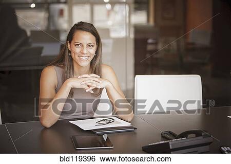 Stock Photograph - Mixed race businesswoman smiling at desk. Fotosearch