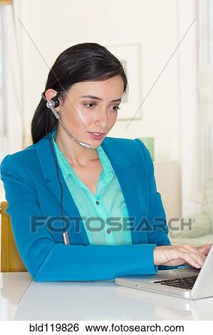 Stock Photograph - Mixed race businesswoman wearing headset and using laptop. Fotosearch