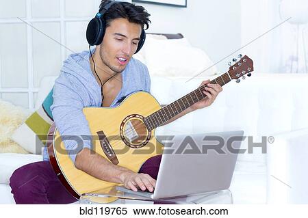 Stock Photography - Mixed race teenager playing guitar and using laptop. Fotosearch