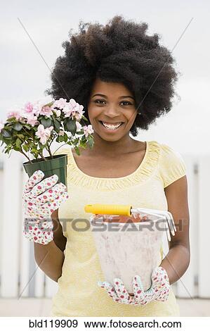Stock Photo - Mixed race woman holding flower and flowerpot. Fotosearch