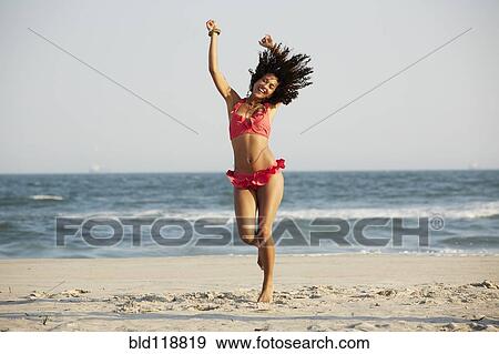 Stock Photo - Mixed race woman jumping for joy on beach. Fotosearch