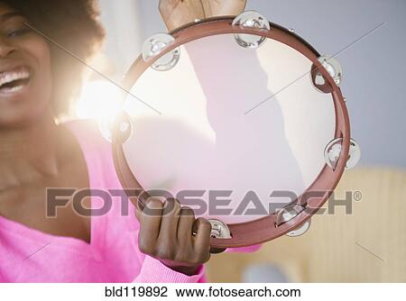 Stock Image - Mixed race woman playing tambourine. Fotosearch