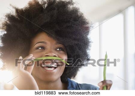 Stock Image - Mixed race woman playing with green beans. Fotosearch