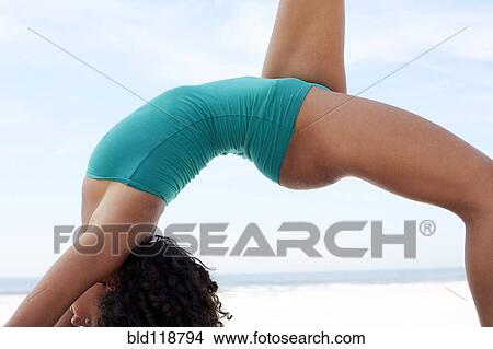 Picture - Mixed race woman practicing yoga on beach. Fotosearch