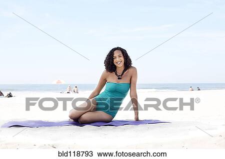 Stock Image - Mixed race woman relaxing on beach. Fotosearch