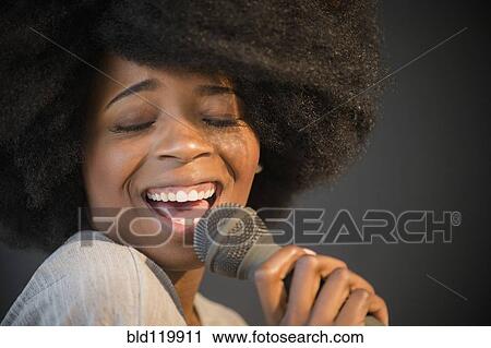 Stock Image - Mixed race woman singing into microphone. Fotosearch