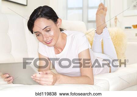 Stock Photo - Mixed race woman using digital tablet on sofa. Fotosearch
