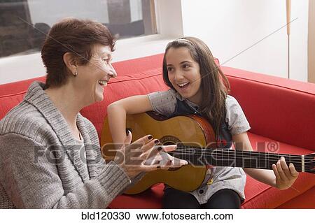 Stock Image - Older Hispanic woman playing music with granddaughter. Fotosearch