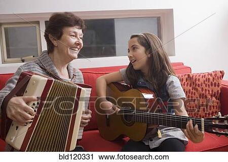 Stock Image - Older Hispanic woman playing music with granddaughter. Fotosearch