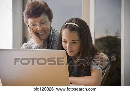 Stock Photograph - Older Hispanic woman using laptop with granddaughter. Fotosearch