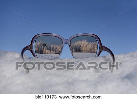 Stock Image - Snow covered trees reflected in sunglasses. Fotosearch