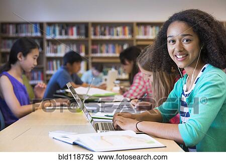 Stock Image - Student using laptop in library. Fotosearch