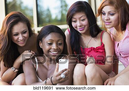 Stock Image - Teenage girls using cell phone together. Fotosearch
