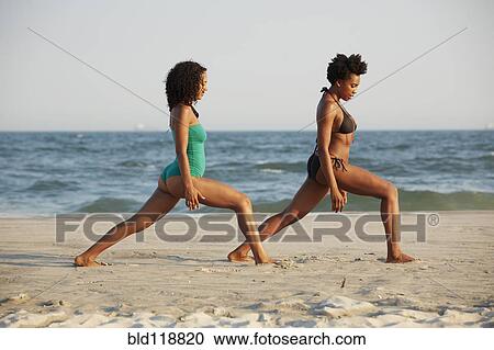 Stock Image - Women practicing yoga on beach. Fotosearch