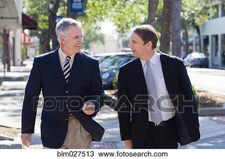 Stock Image - Caucasian businessmen walking on city street. Fotosearch