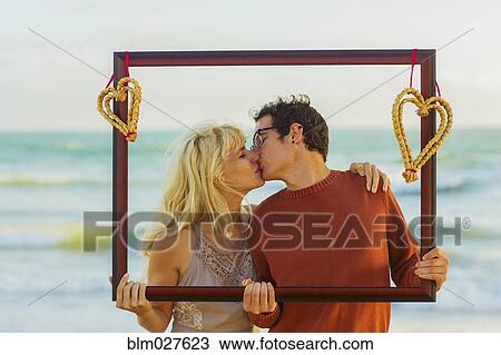 Stock Image - Caucasian couple holding frame with hearts and kissing. Fotosearch