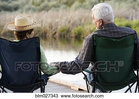 Stock Image - Caucasian couple relaxing in chairs on dock. Fotosearch