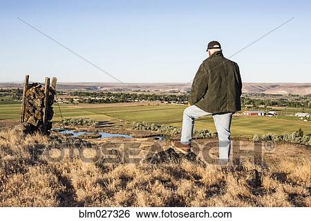 Stock Photograph - Caucasian farmer looking over fields. Fotosearch