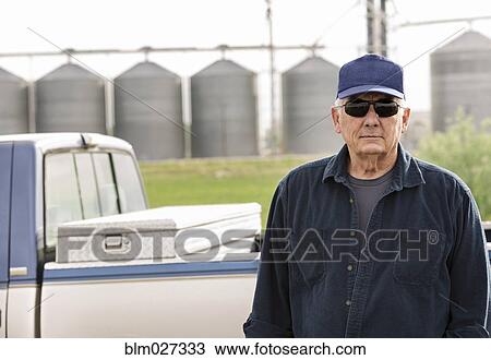 Stock Image - Caucasian farmer standing by truck. Fotosearch