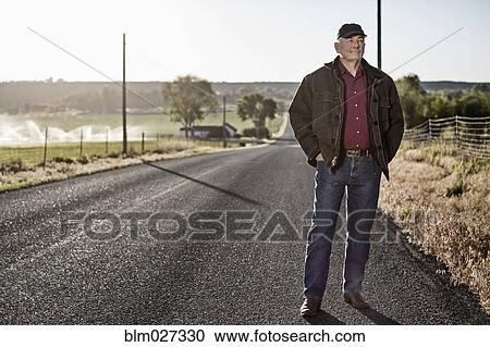 Stock Image - Caucasian farmer standing on rural road. Fotosearch