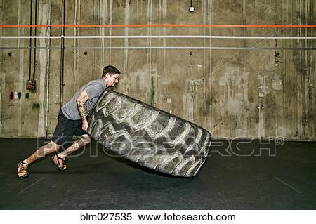 Stock Photography - Caucasian man lifting large tire in gym. Fotosearch