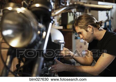Stock Image - Caucasian mechanic working on motorcycle. Fotosearch