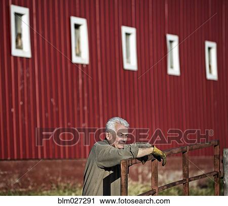 Stock Image - Caucasian rancher standing by barn. Fotosearch