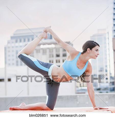 Stock Image - Caucasian woman practicing yoga on urban rooftop. Fotosearch
