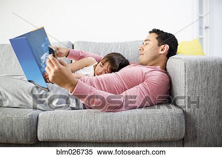 Stock Photography - Father and daughter reading together on sofa. Fotosearch