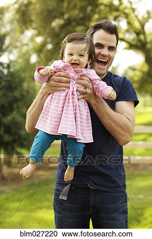 Father holding toddler daughter in park View Large Photo Image Stock Image - Father holding toddler daughter in park. Fotosearch