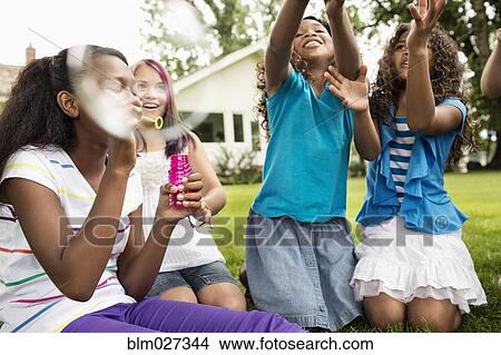 Girls blowing bubbles in backyard View Large Photo Image Picture - Girls blowing bubbles in backyard. Fotosearch